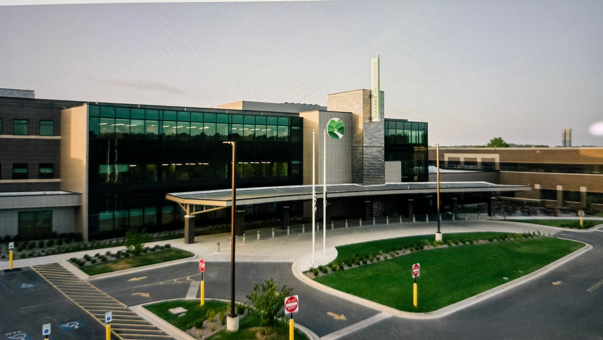 Modern hospital exterior with glass facade, covered entrance, and circular driveway at dusk