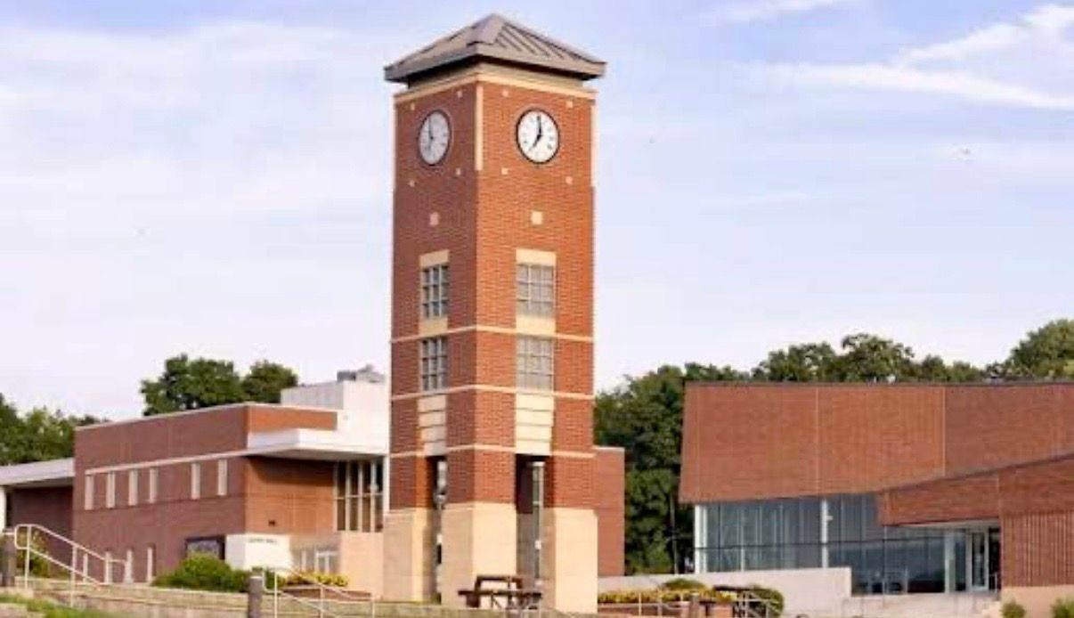 Brick clock tower on a campus building with red-roofed wings and a clear sky background