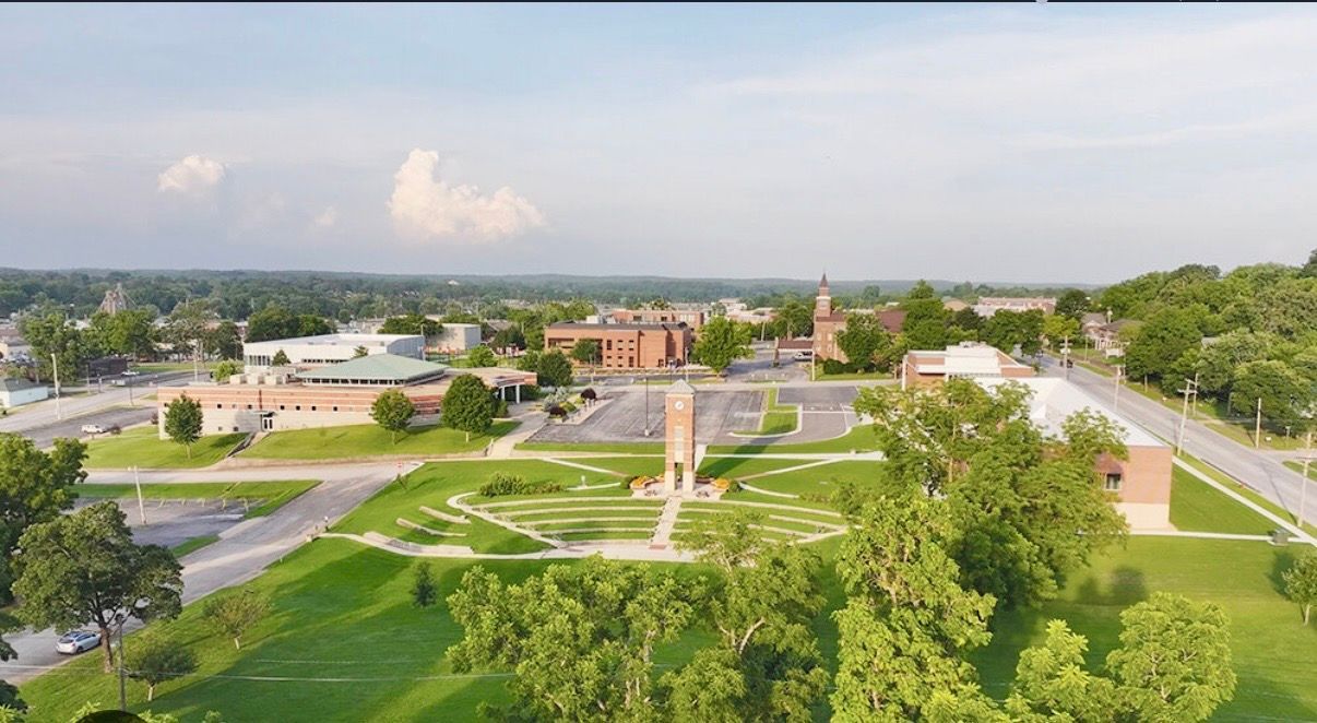 Aerial view of a green campus with pathways, buildings, and a central brick tower under a clear sky