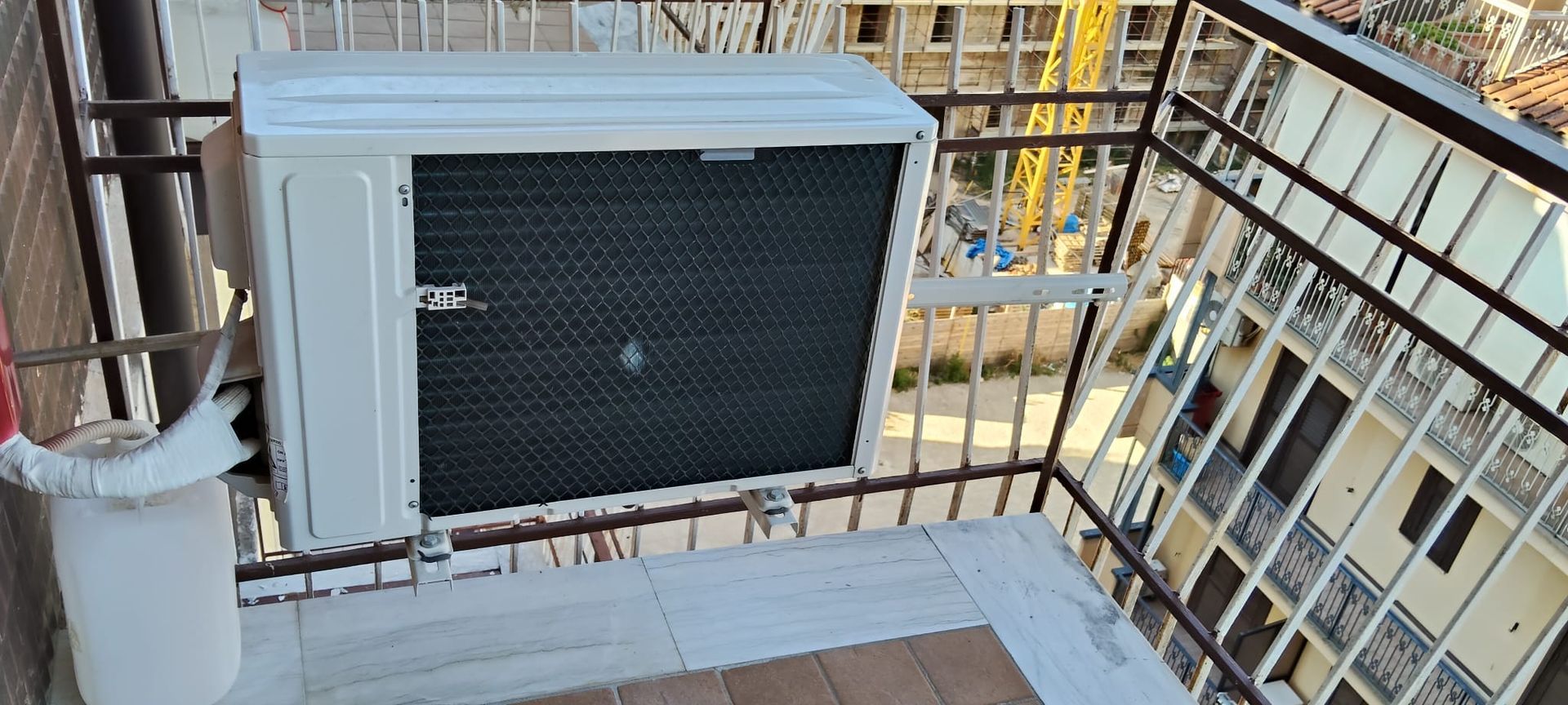 Un condizionatore bianco è posizionato su un balcone accanto a un edificio.