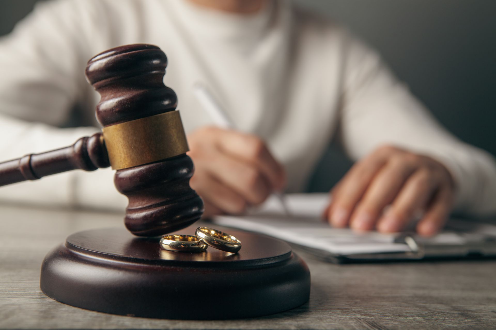 Gavel and wedding rings on a desk with a blurred person writing in the background