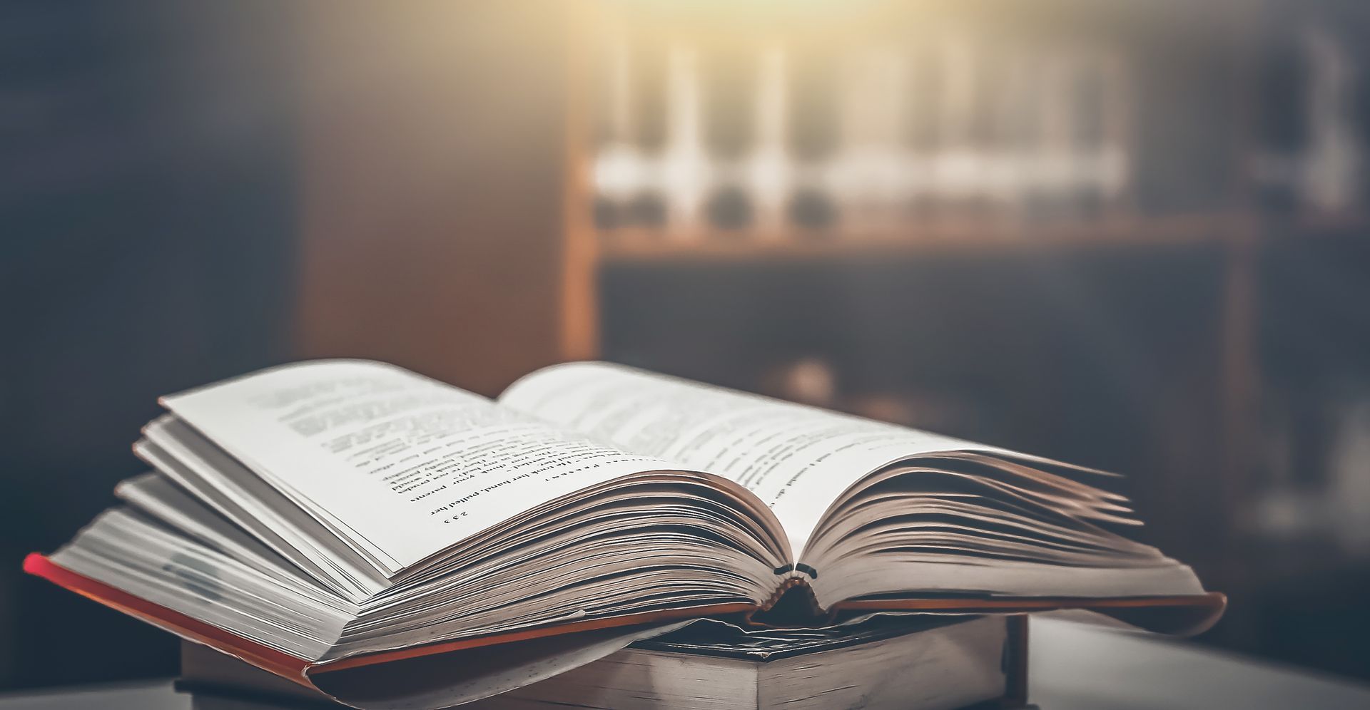 Open book on a table in a softly lit library, with blurred shelves in the background