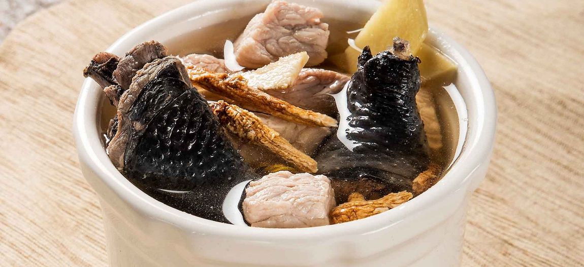 Close-up of a cup of fish soup with chunks of fish and a lemon wedge