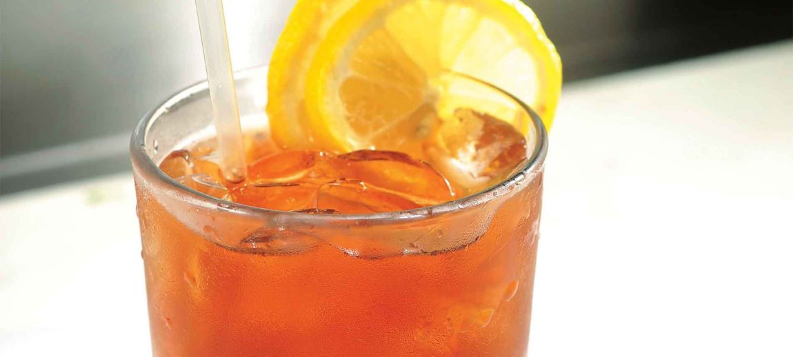 Orange iced drink with a lemon slice and straw in a clear glass