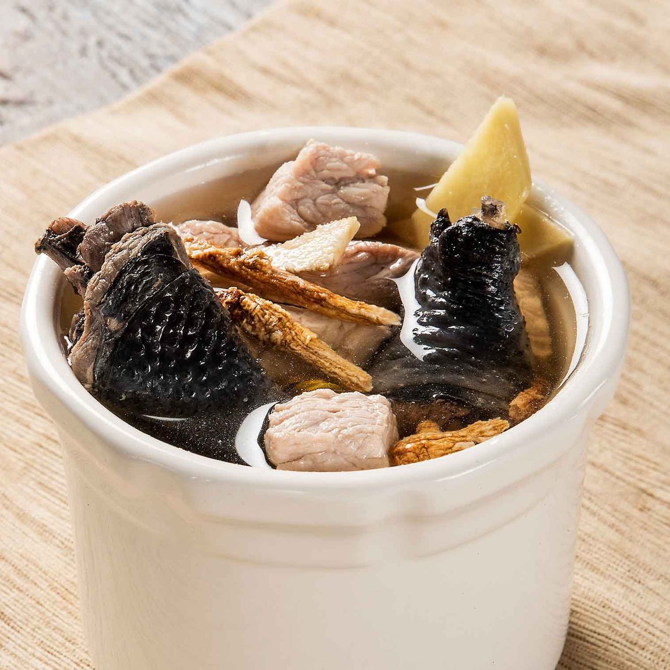 White mug filled with dark tea, ginger, and fruit slices on a light wooden table