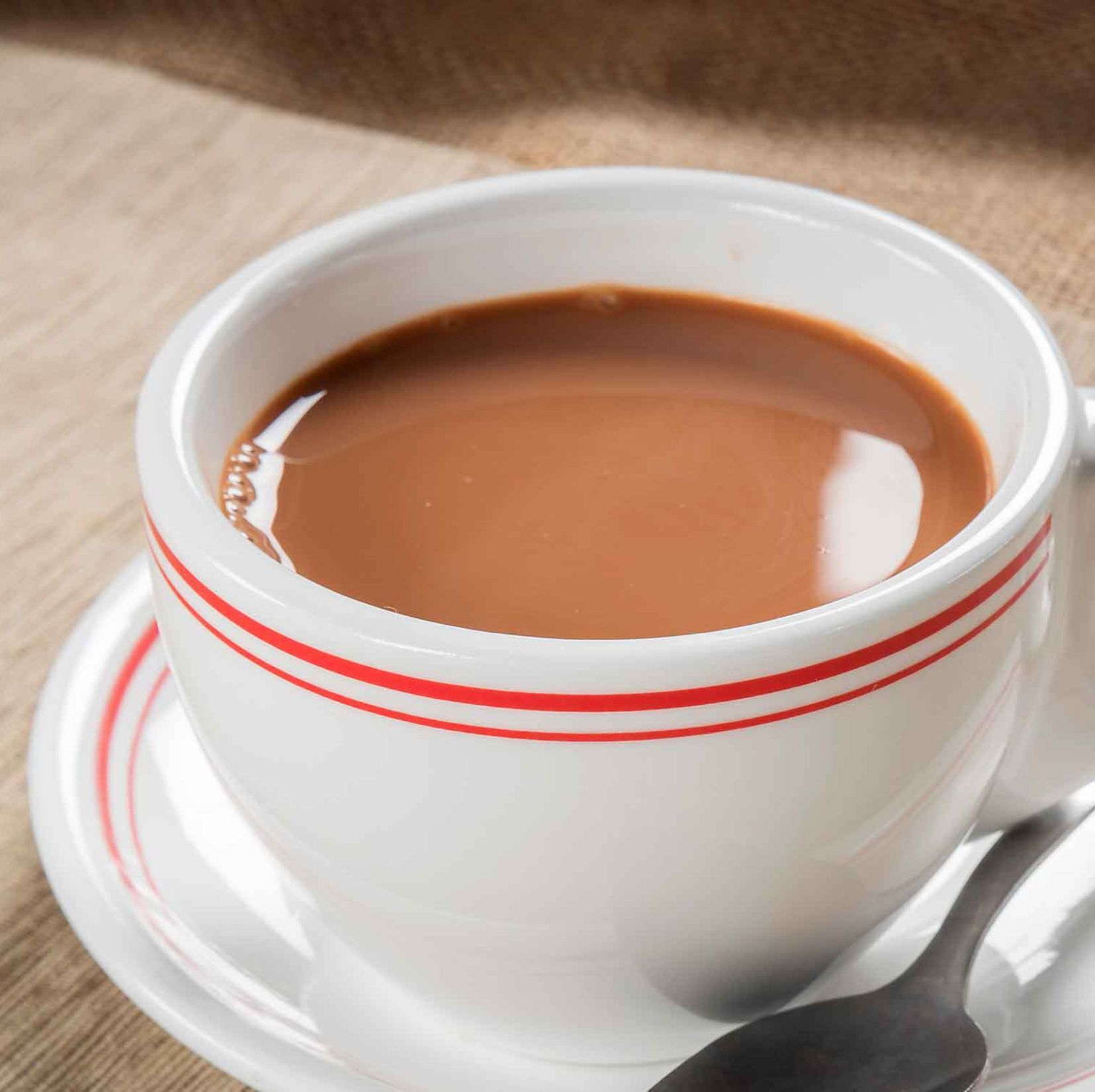White cup of coffee with red stripes on a saucer and spoon on a wooden table
