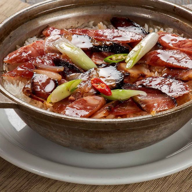 Braised meat in a brown bowl, garnished with green onions and red chili peppers