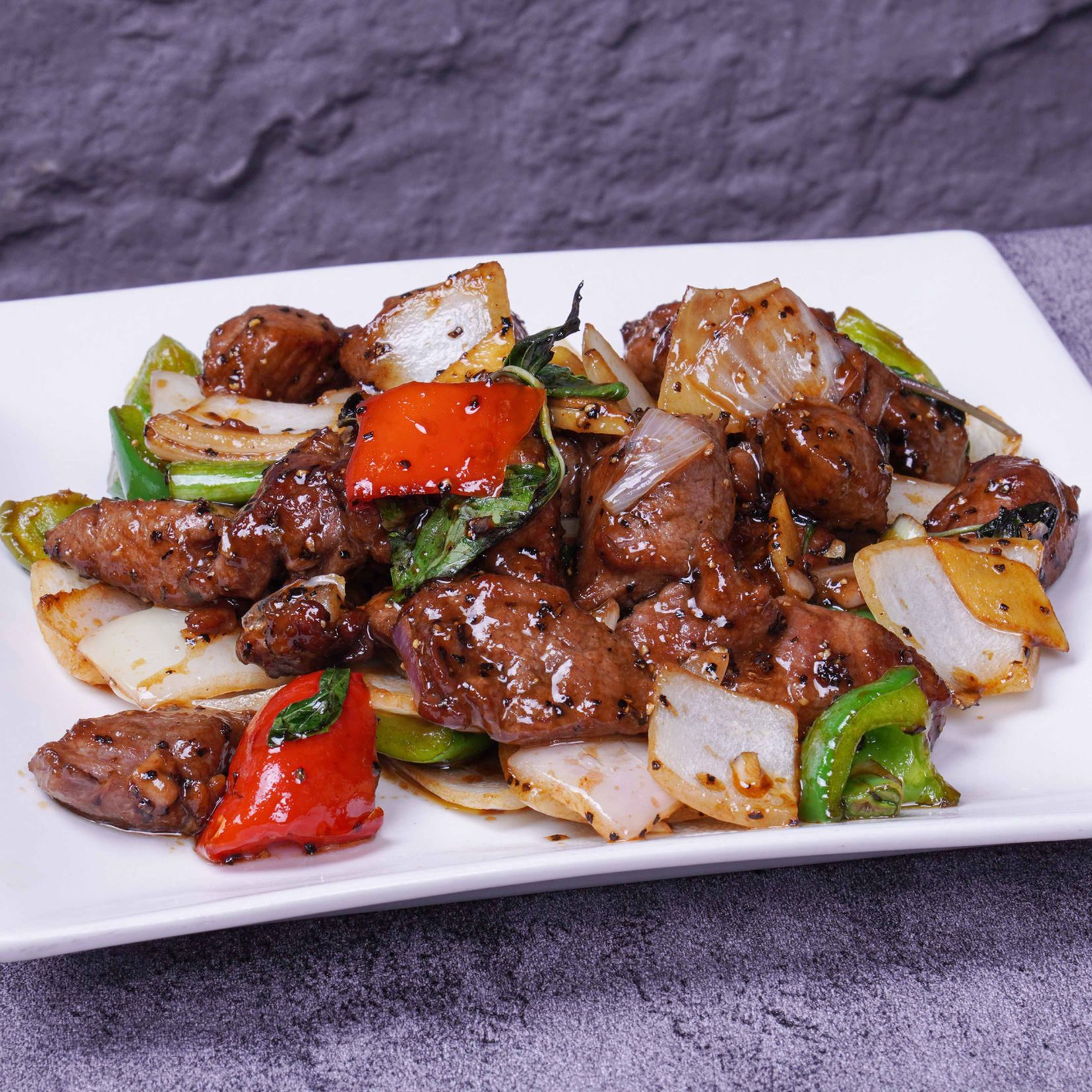 Stir-fried beef with peppers and onions on a white rectangular plate