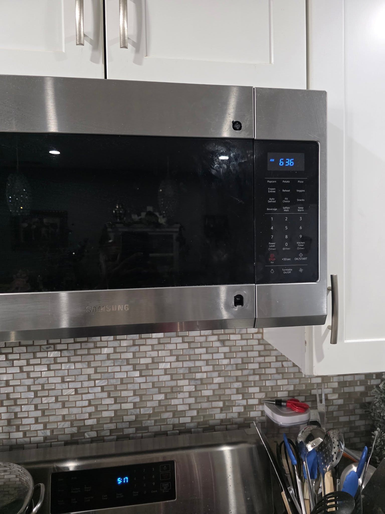 Stainless steel microwave above stove in a kitchen with white cabinets and a mosaic tile backsplash