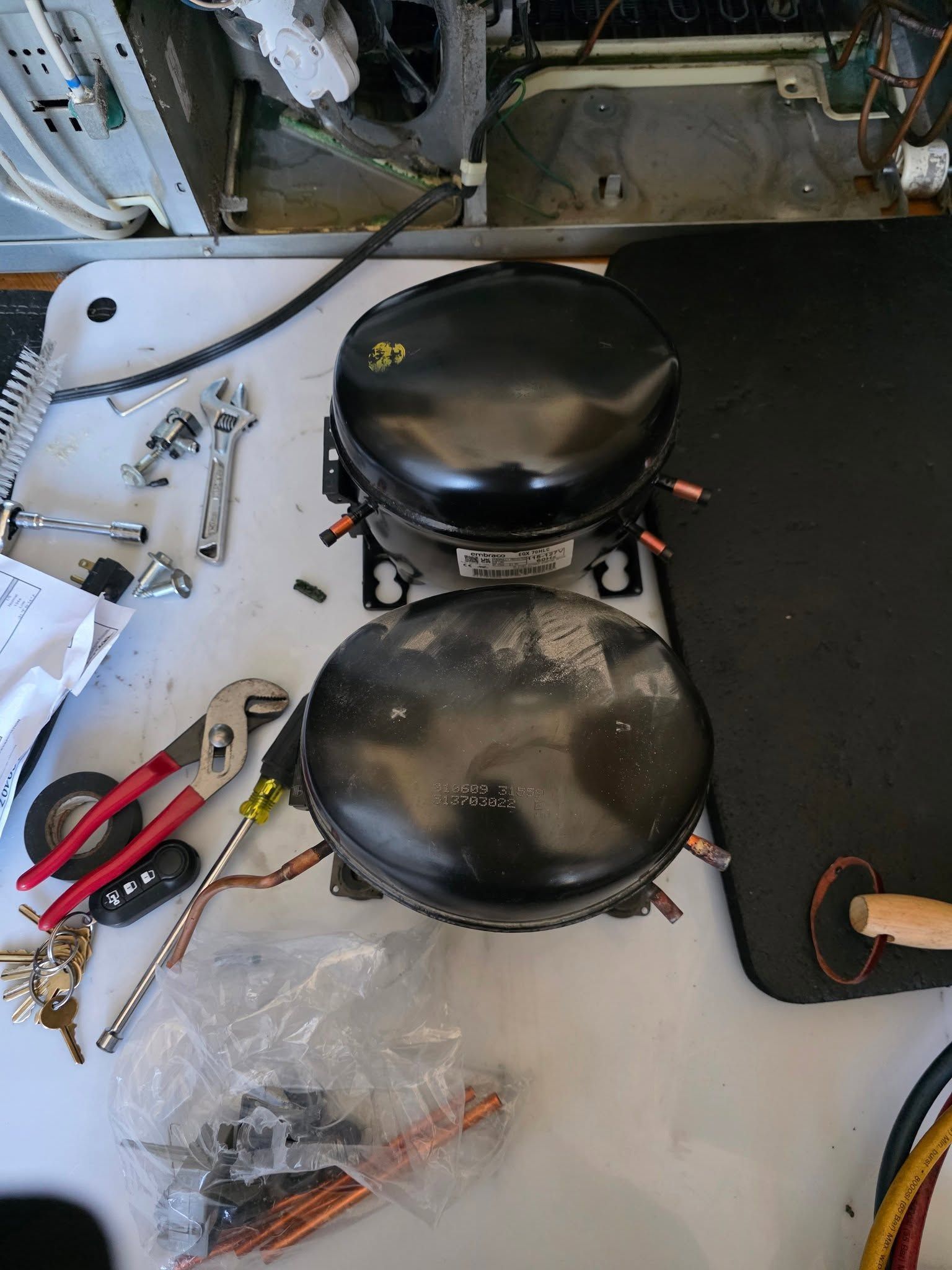 Two black round compressor tanks on a white workbench with pliers, screws, and tools nearby
