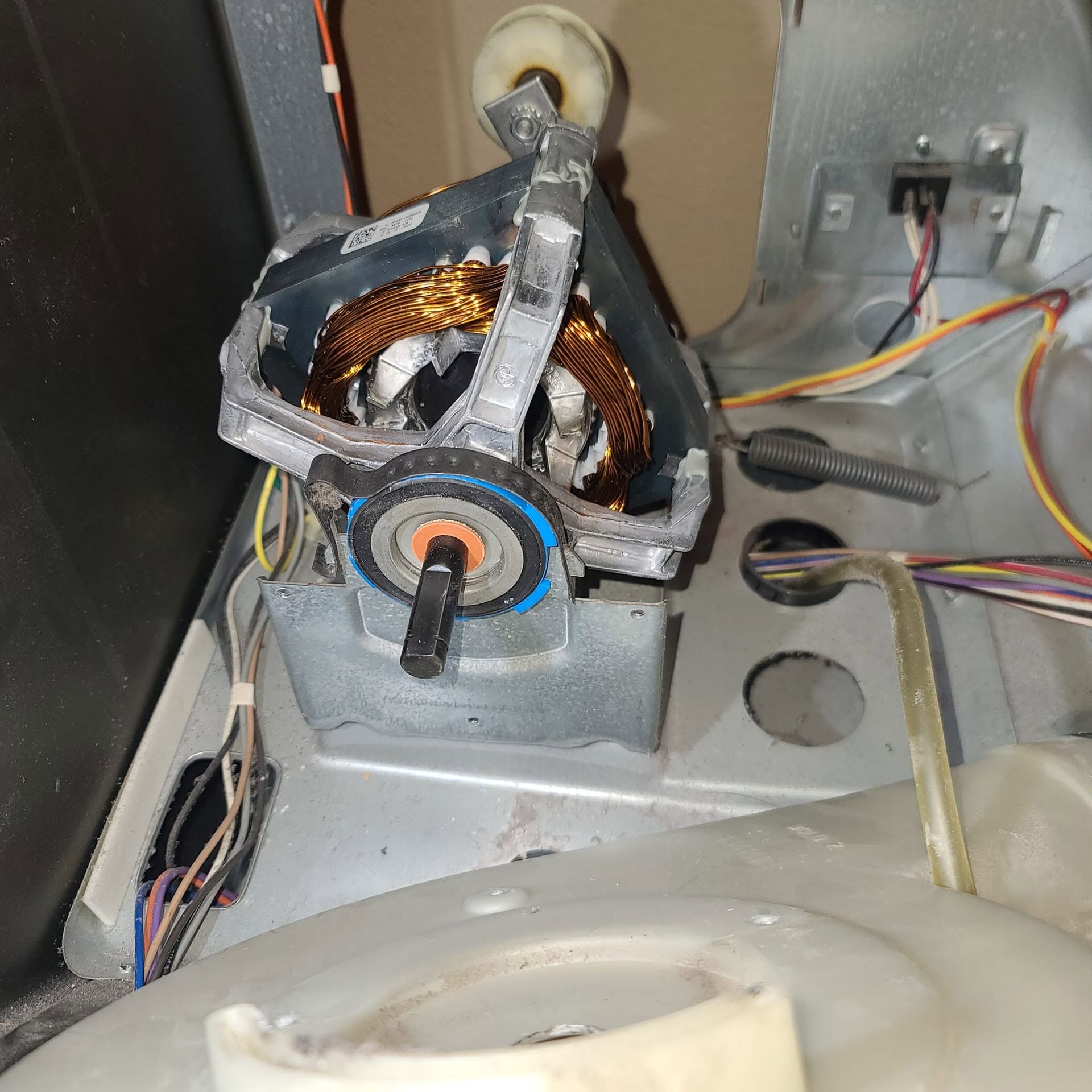 Damaged electric motor with exposed copper windings inside a metal appliance housing.