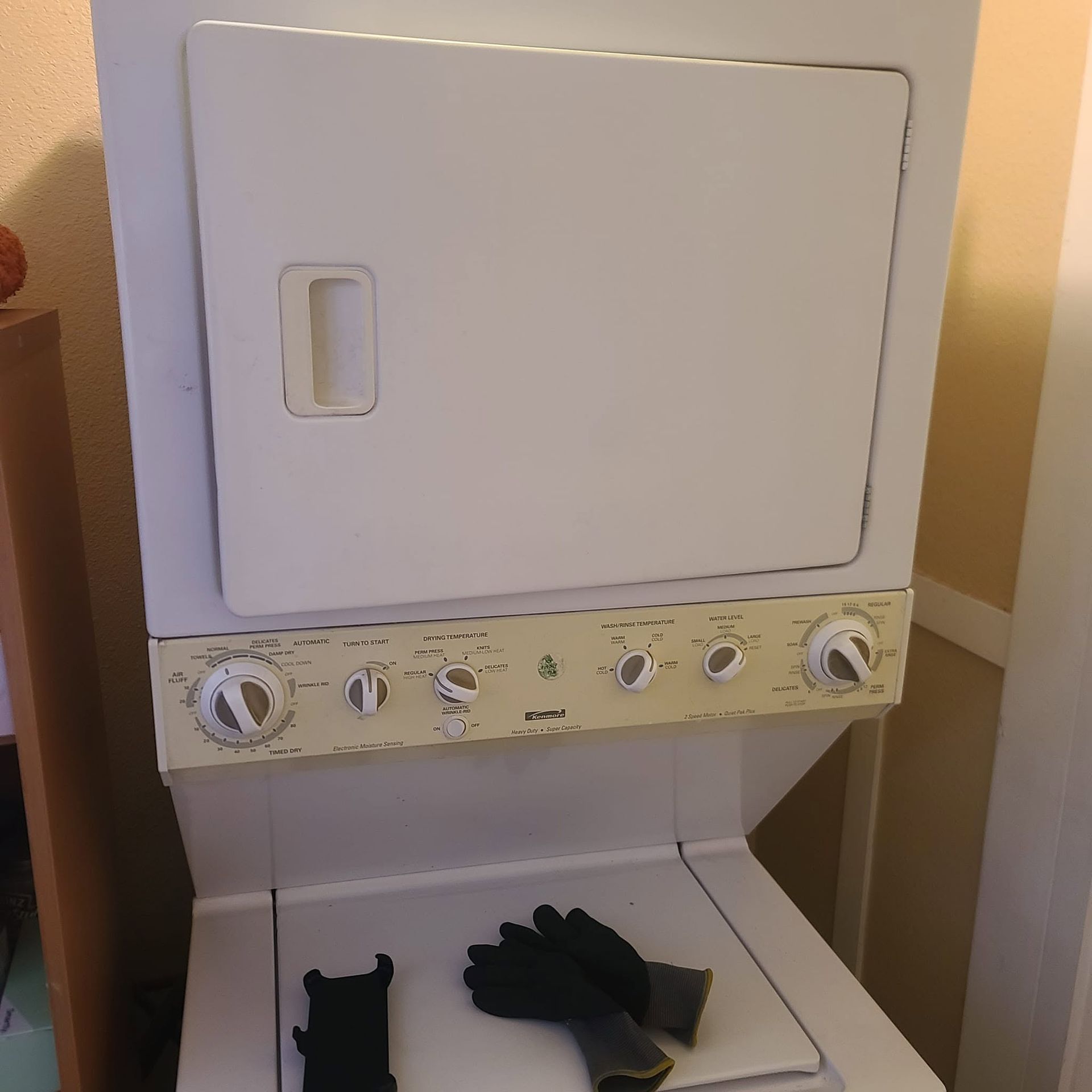 White stacked washer and dryer with front control panel and two black gloves on the open washer door