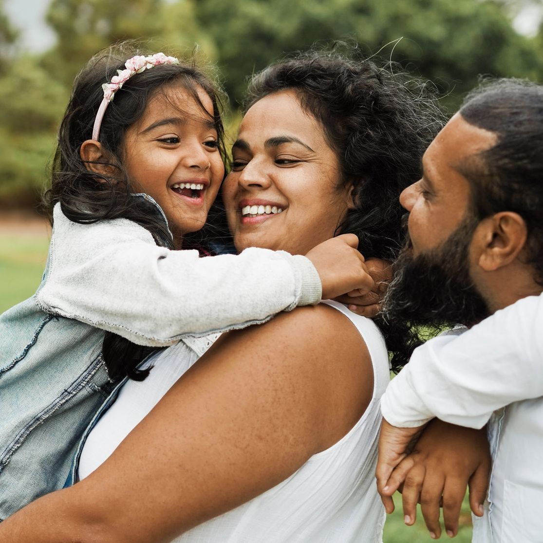 Woman holding a laughing child, man smiling nearby, outdoors.