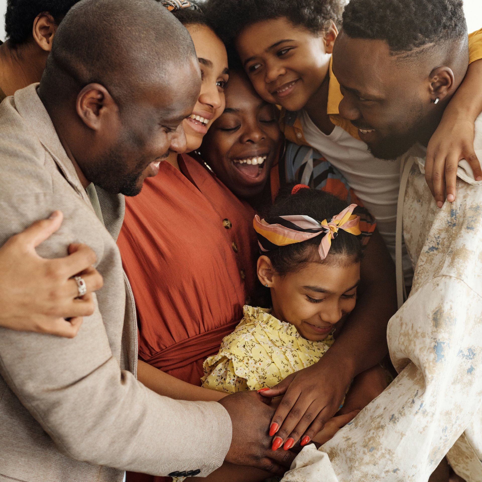 Group of people embracing, smiling. Several are wearing neutral and warm-toned clothing.