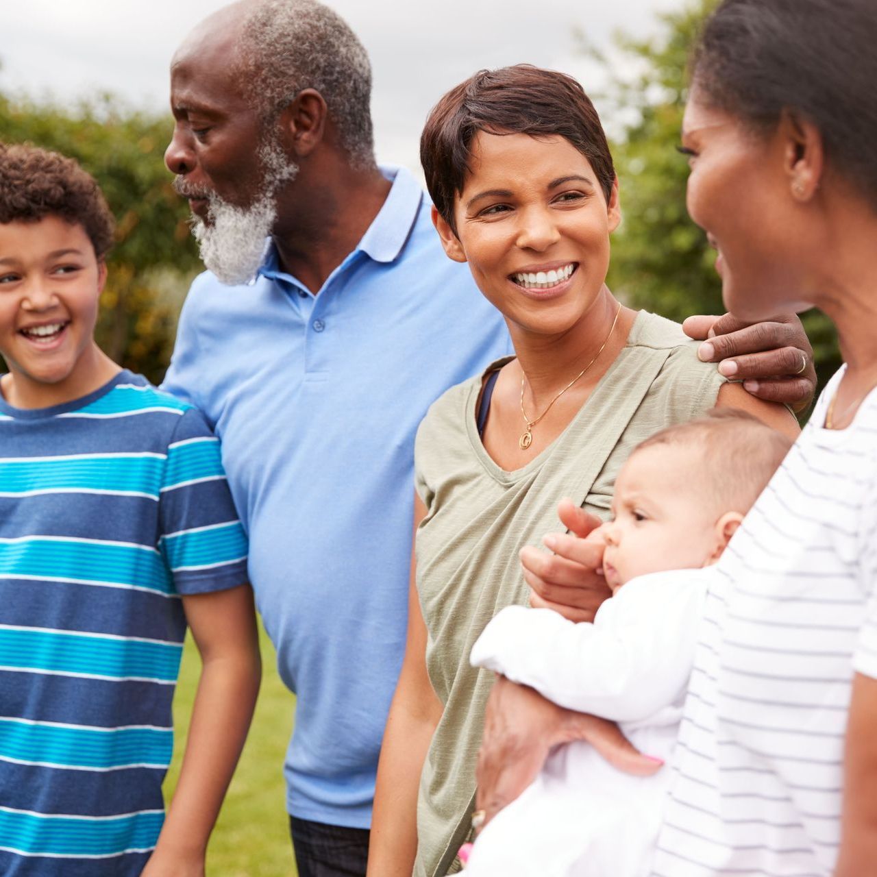 Family outdoors, smiling and talking; child, baby, and grandparents.