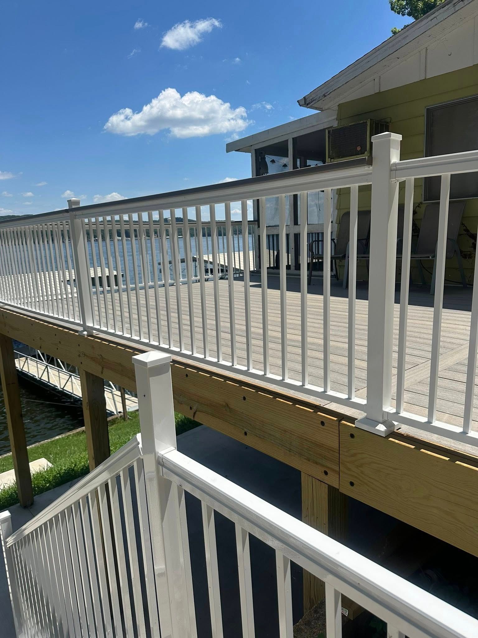 White railing on a wooden deck overlooking a body of water under a blue sky.