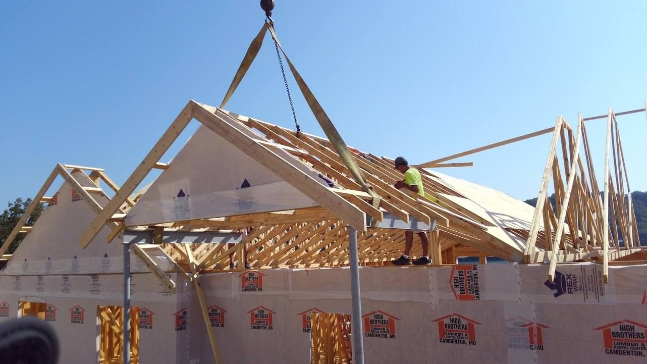Construction workers placing roof trusses on a building frame using a crane. Clear blue sky.