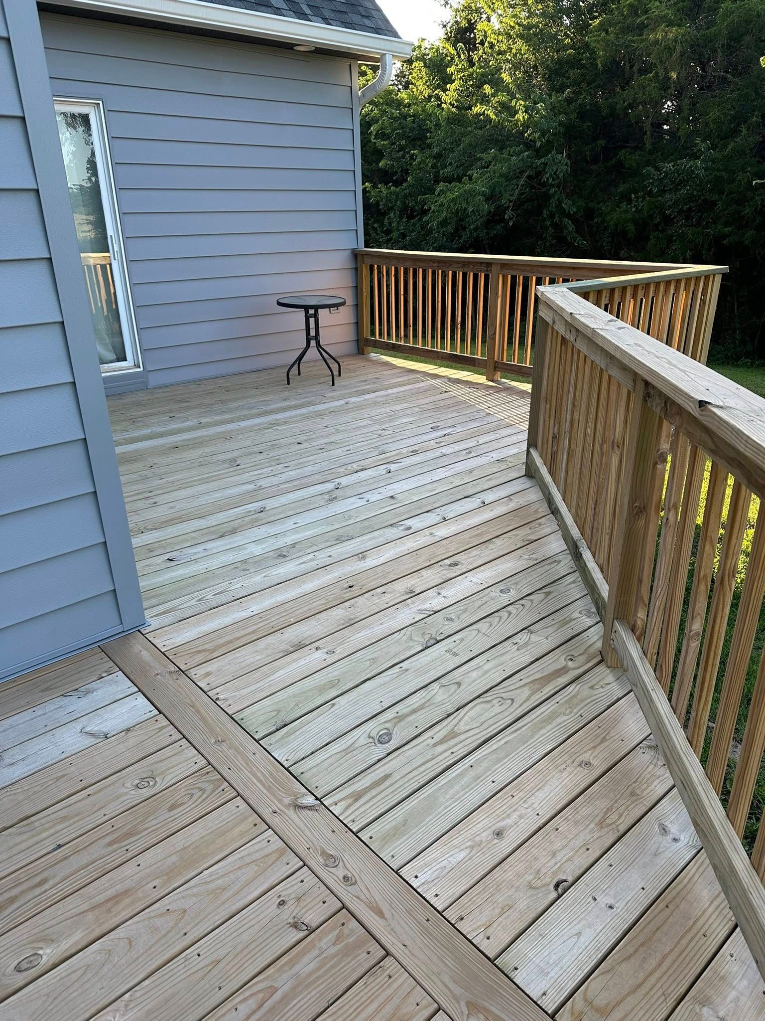 Wooden deck attached to a gray house, with a railing and small table.