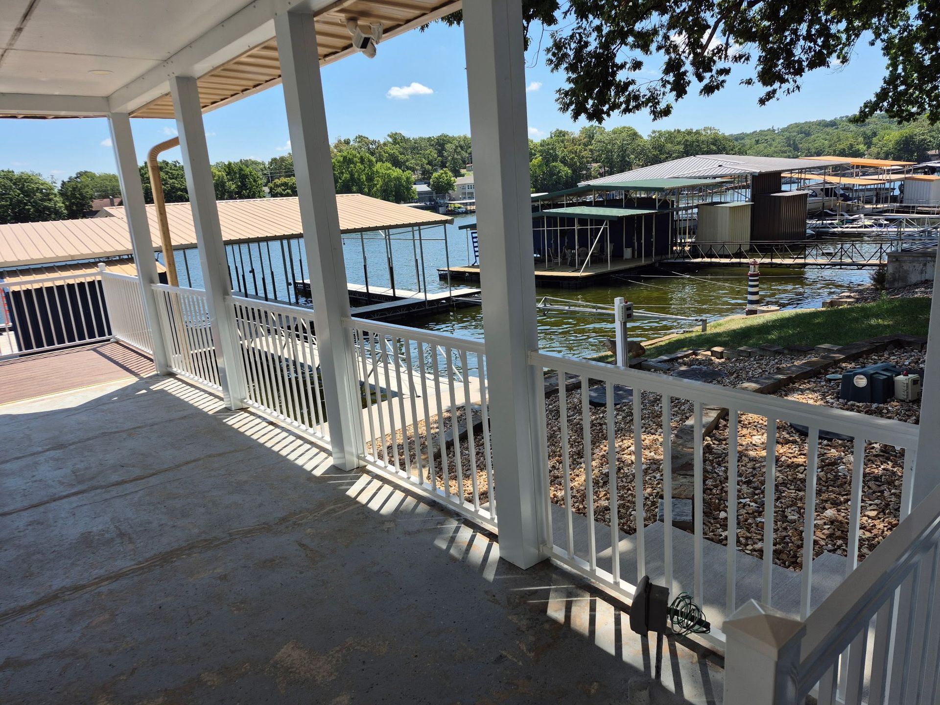 View from a white porch with railings overlooking a lake and boat docks on a sunny day.