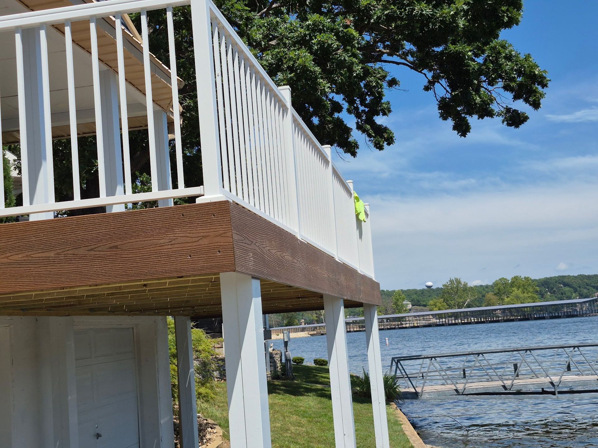 White deck with brown trim overlooking a lake, blue sky, and trees.