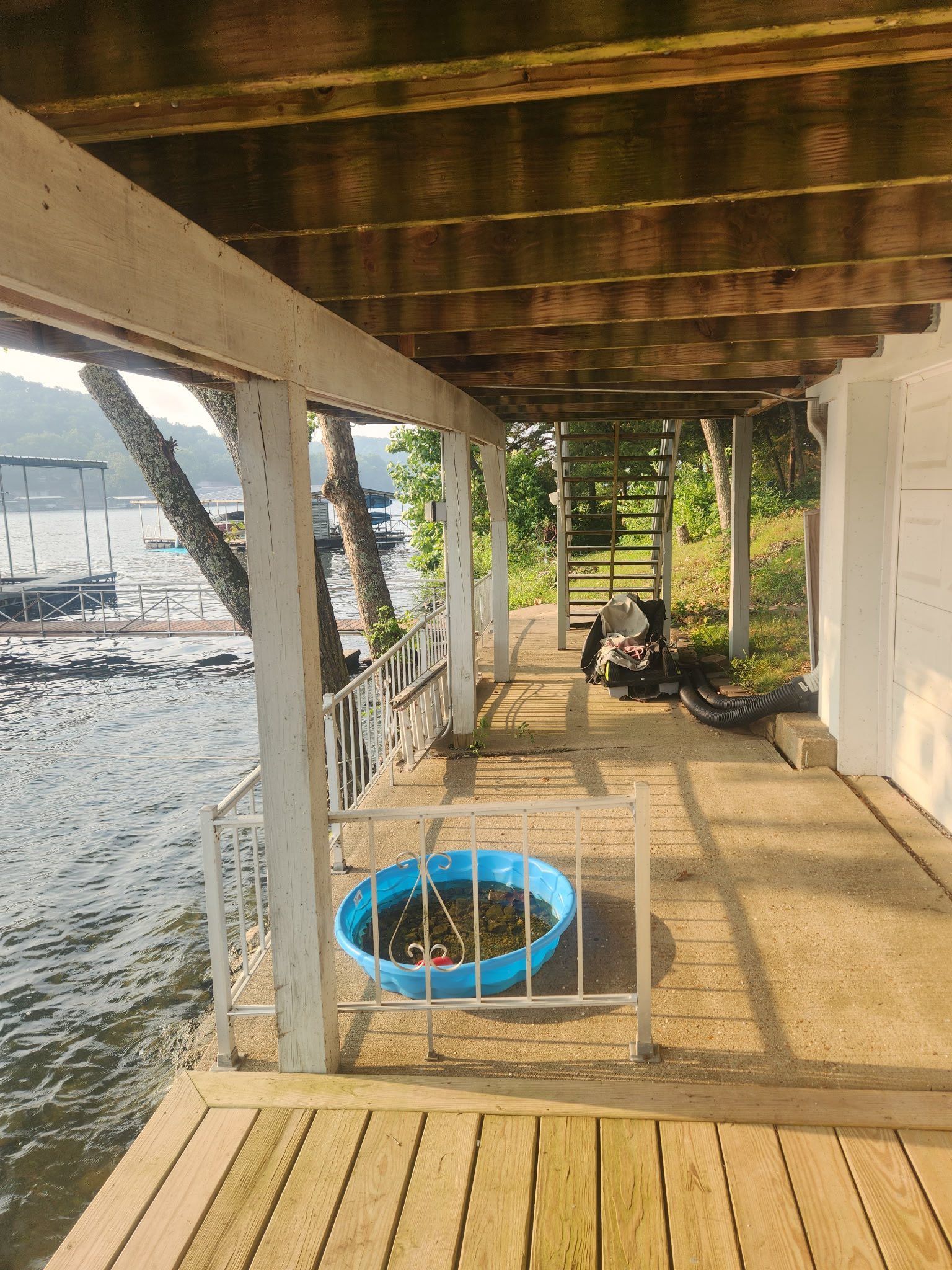 Wooden deck overlooking water, with blue kiddie pool and railing.