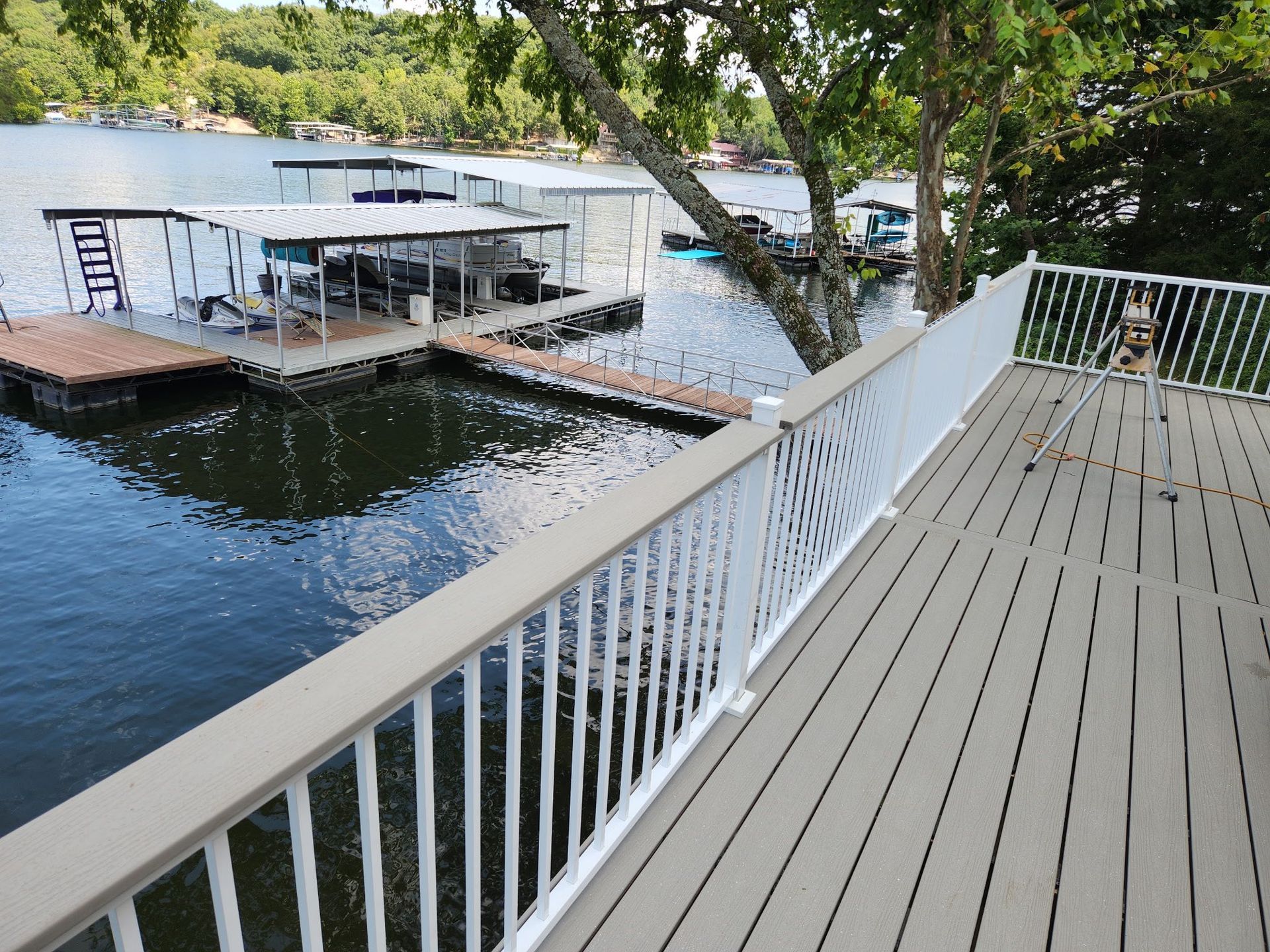 Deck overlooking a lake with docks and boat houses. White railing, gray decking, blue water, trees in the background.