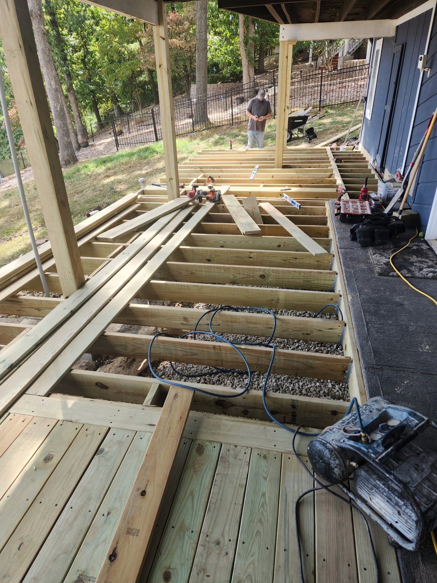 Deck under construction with exposed joists, tools, and a person in the background.
