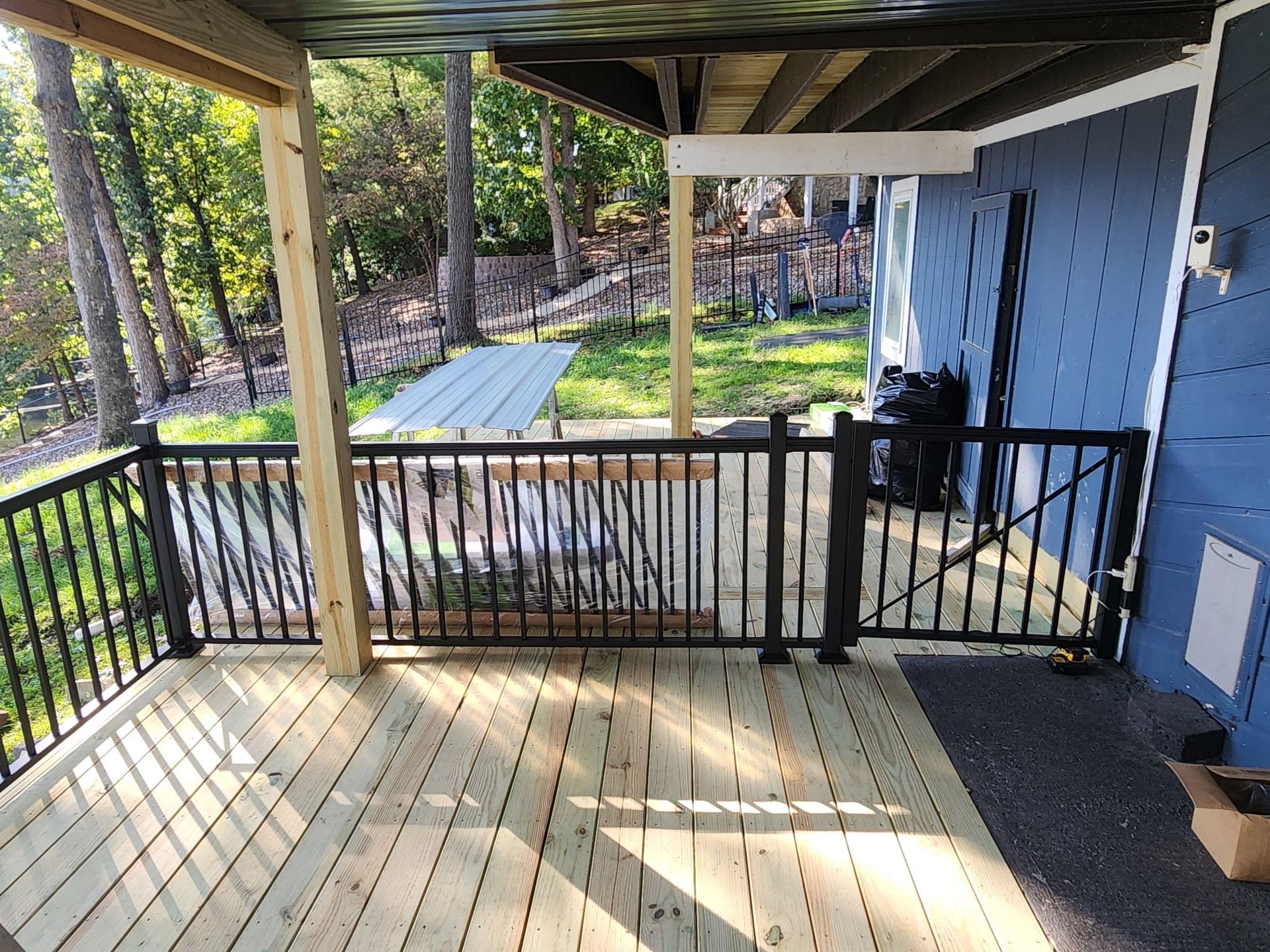 Wooden deck with black railings, partially covered, overlooking a yard with trees.