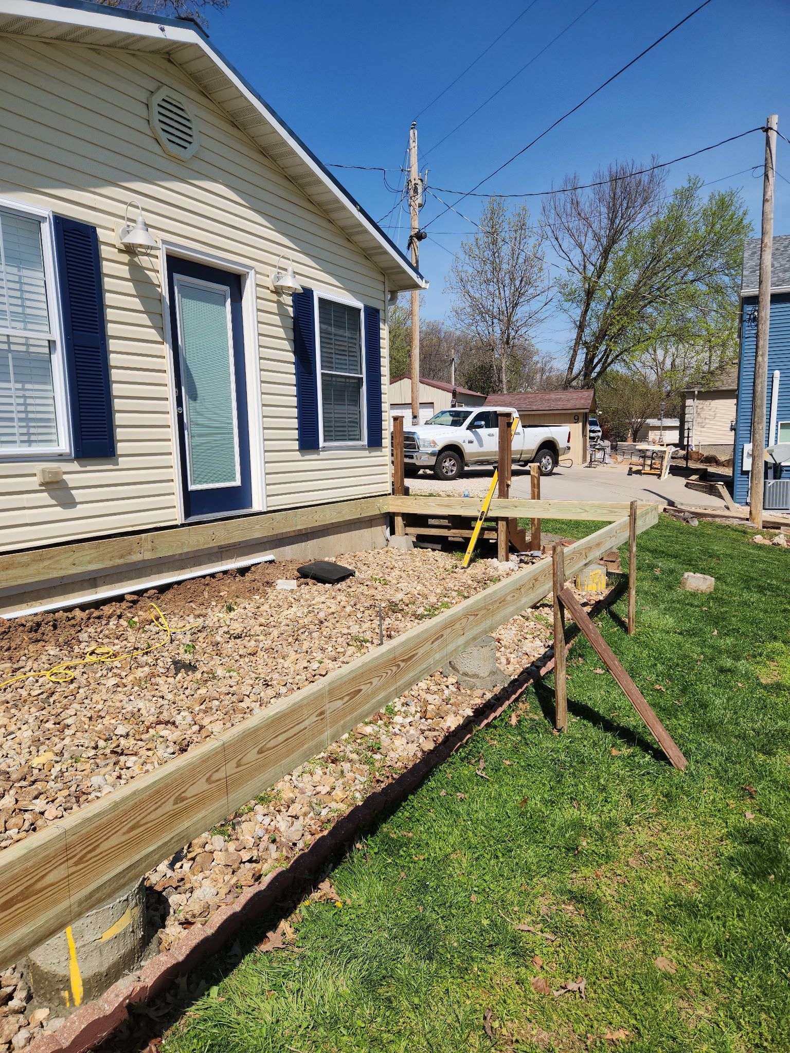 Wooden ramp under construction beside a house, with a worker, tools, and a truck in the background