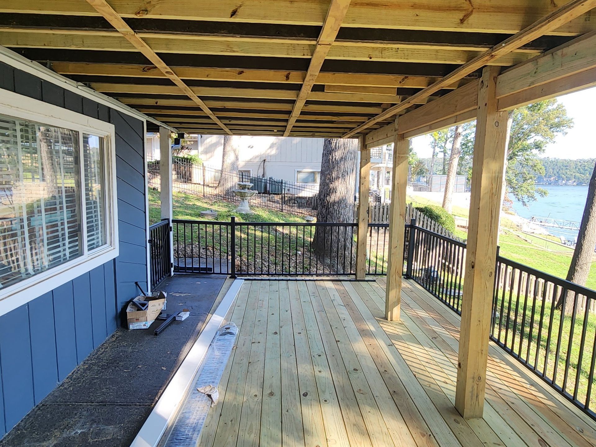 Covered wooden porch with blue siding, railing, and lake view beyond the deck.