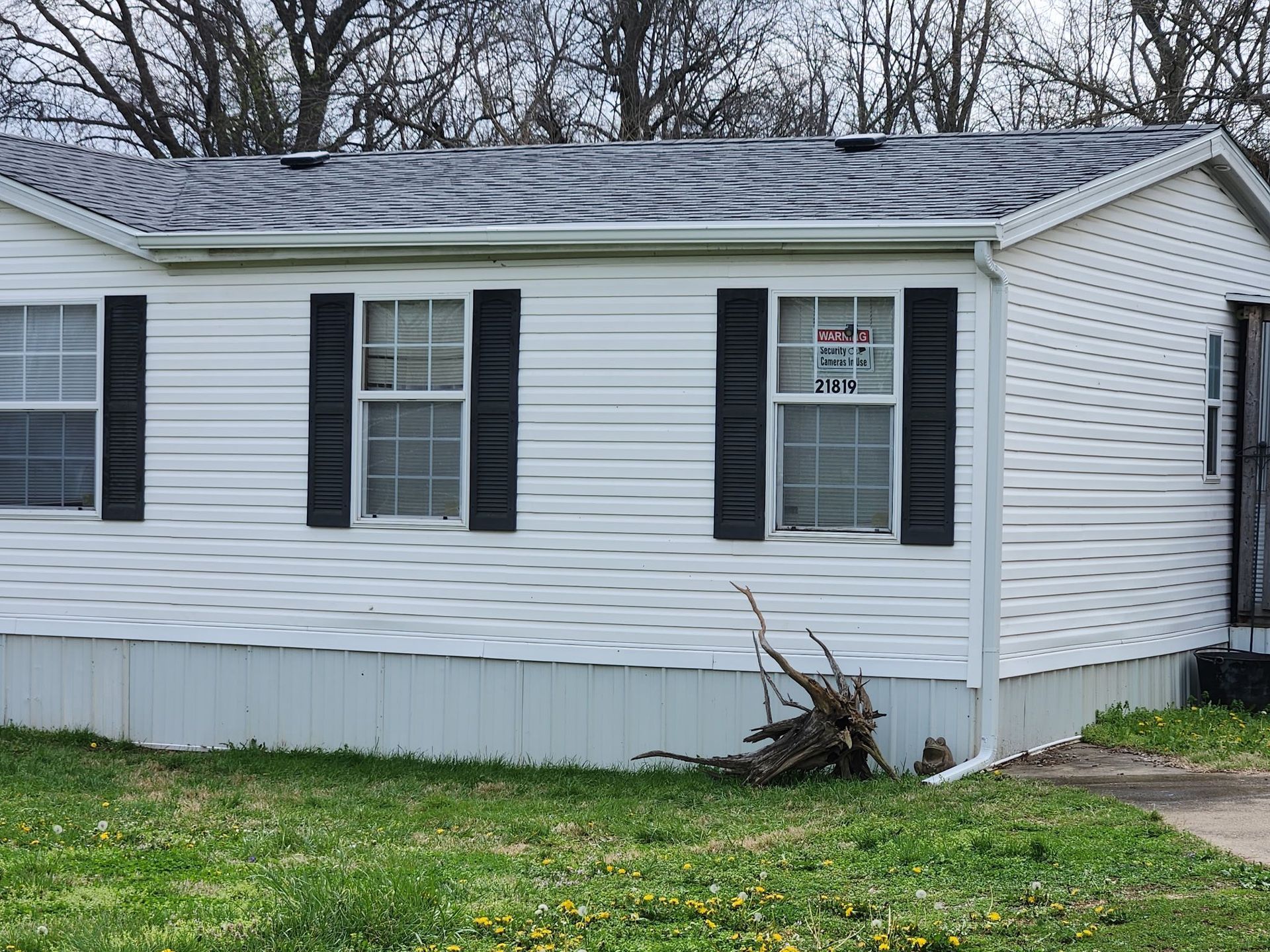 White house with black shutters and a damaged front siding panel near the lawn.