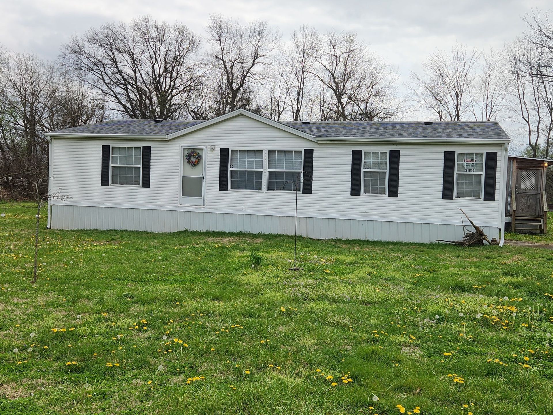 White single-story mobile home with green shutters and a small front porch in a grassy yard.