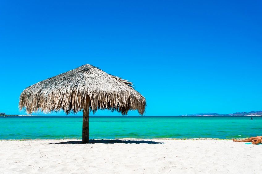 There is a thatched umbrella on the beach near the ocean.