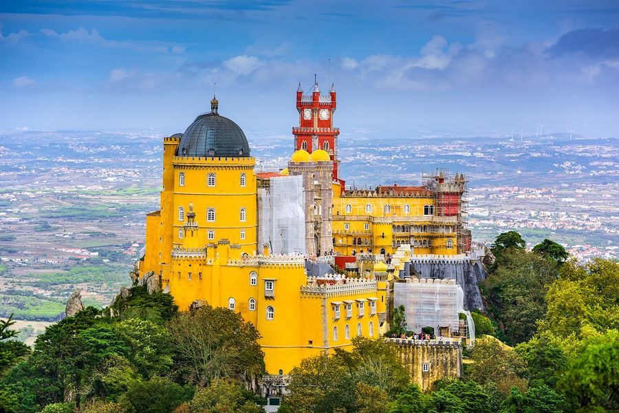 A large yellow castle is sitting on top of a hill surrounded by trees.