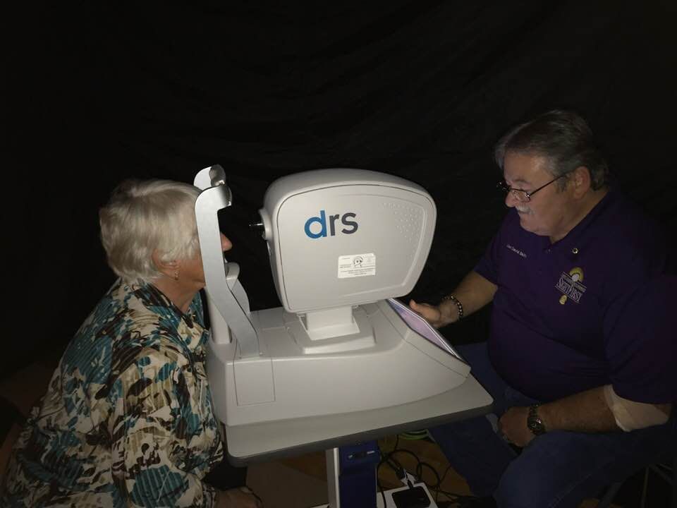 A man is examining a woman 's eye with a machine that says drs on it.