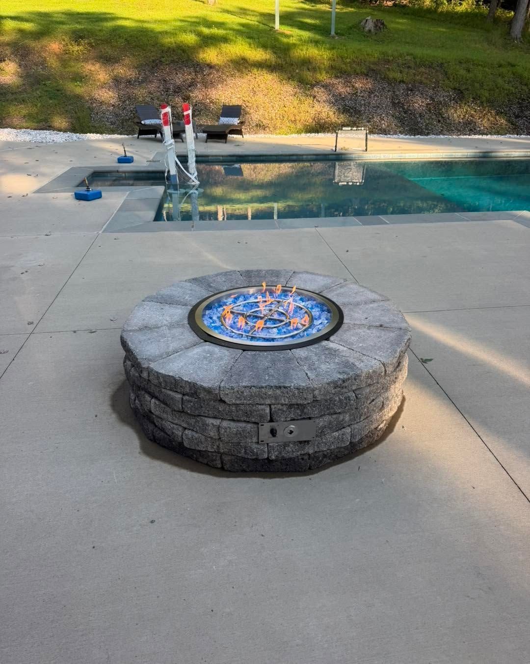 Stone fire pit beside a swimming pool, with flames visible in the center.