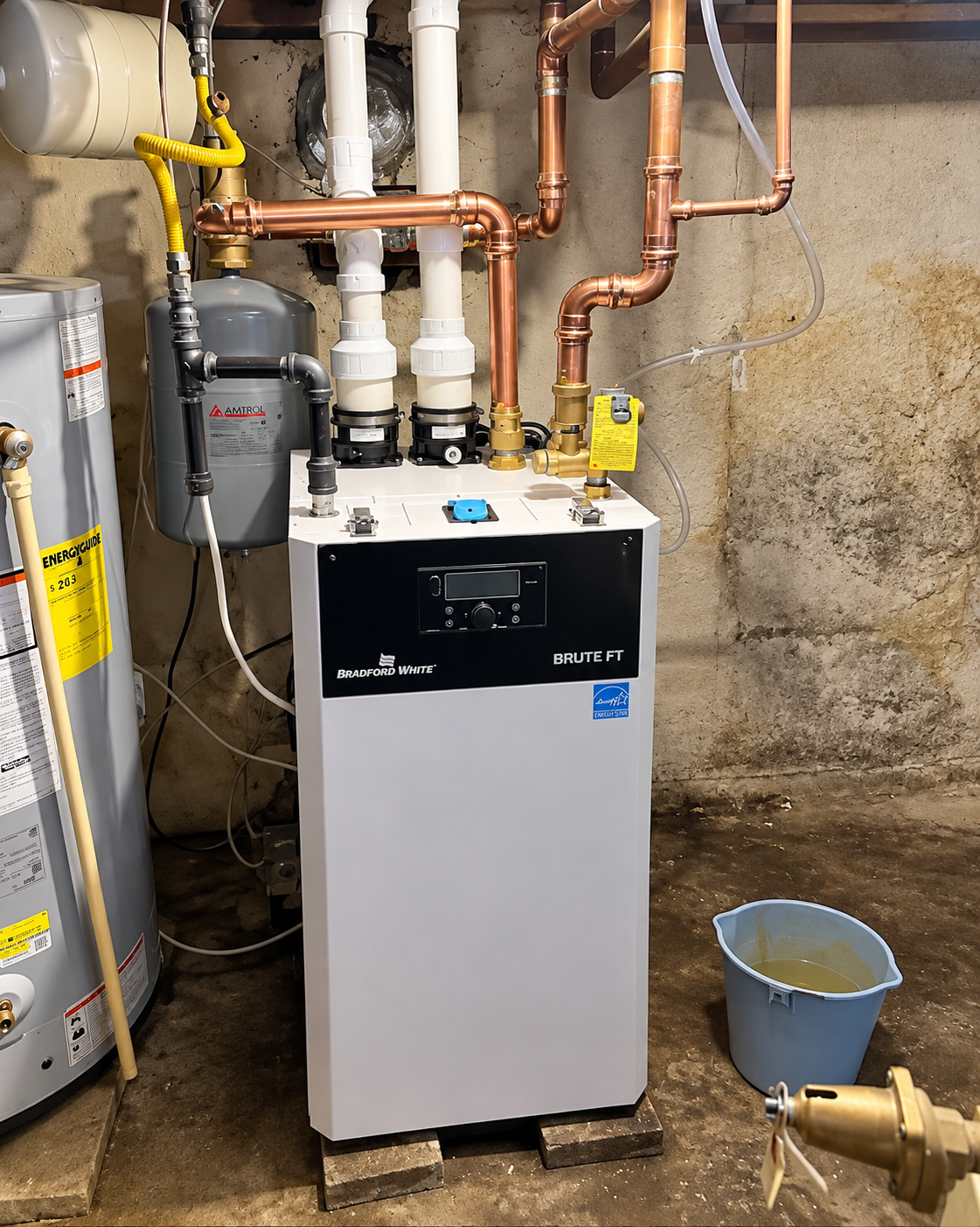 White boiler unit in a utility room with copper pipes, valves, and a bucket on the floor.
