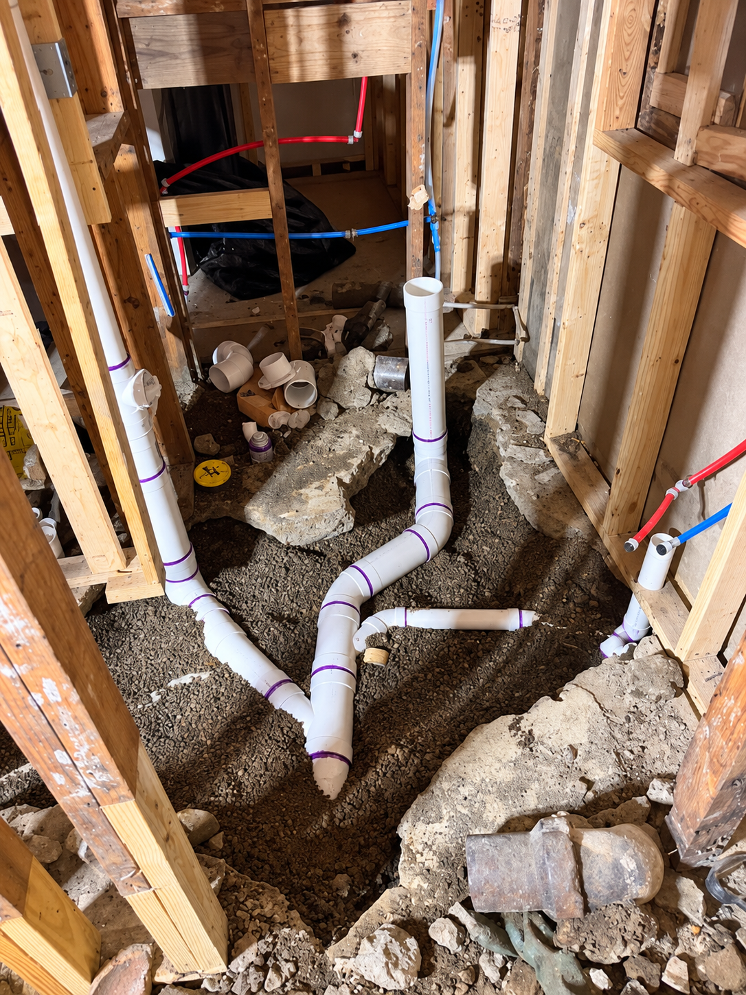 Exposed plumbing in a construction site bathroom, with white PVC pipes and unfinished walls and floor.