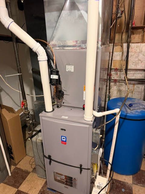 Basement furnace and water heater with white PVC pipes and blue utility barrel.