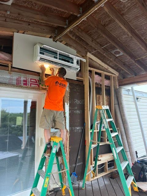 Worker installing a wall-mounted mini-split AC unit on a porch under construction
