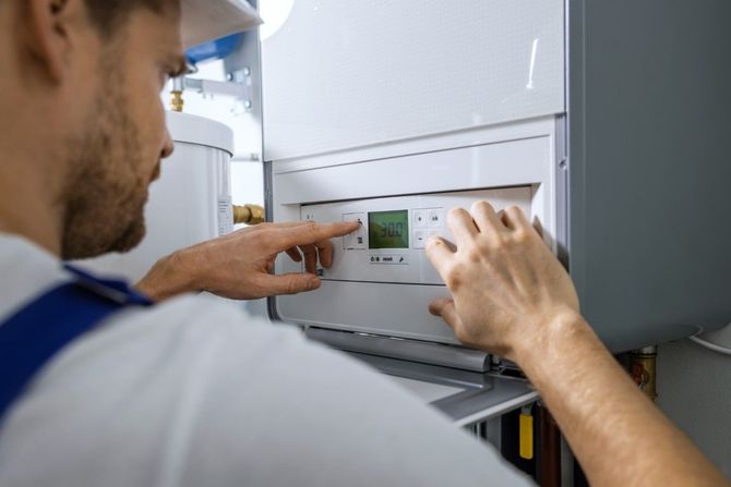 Technician adjusting controls on a wall-mounted boiler with a digital display