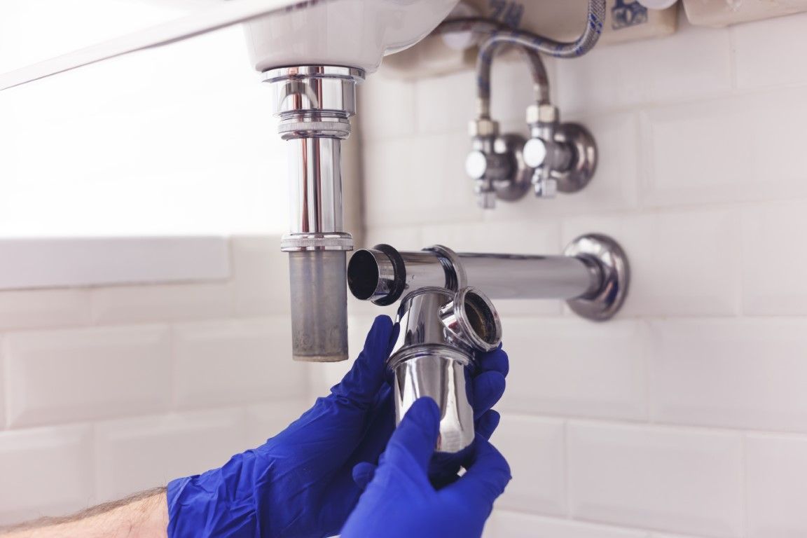Gloved hands fixing a chrome sink drain under a bathroom sink