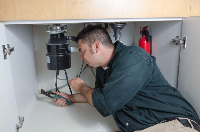 Technician repairing pipes under a sink with tools in a cabinet.