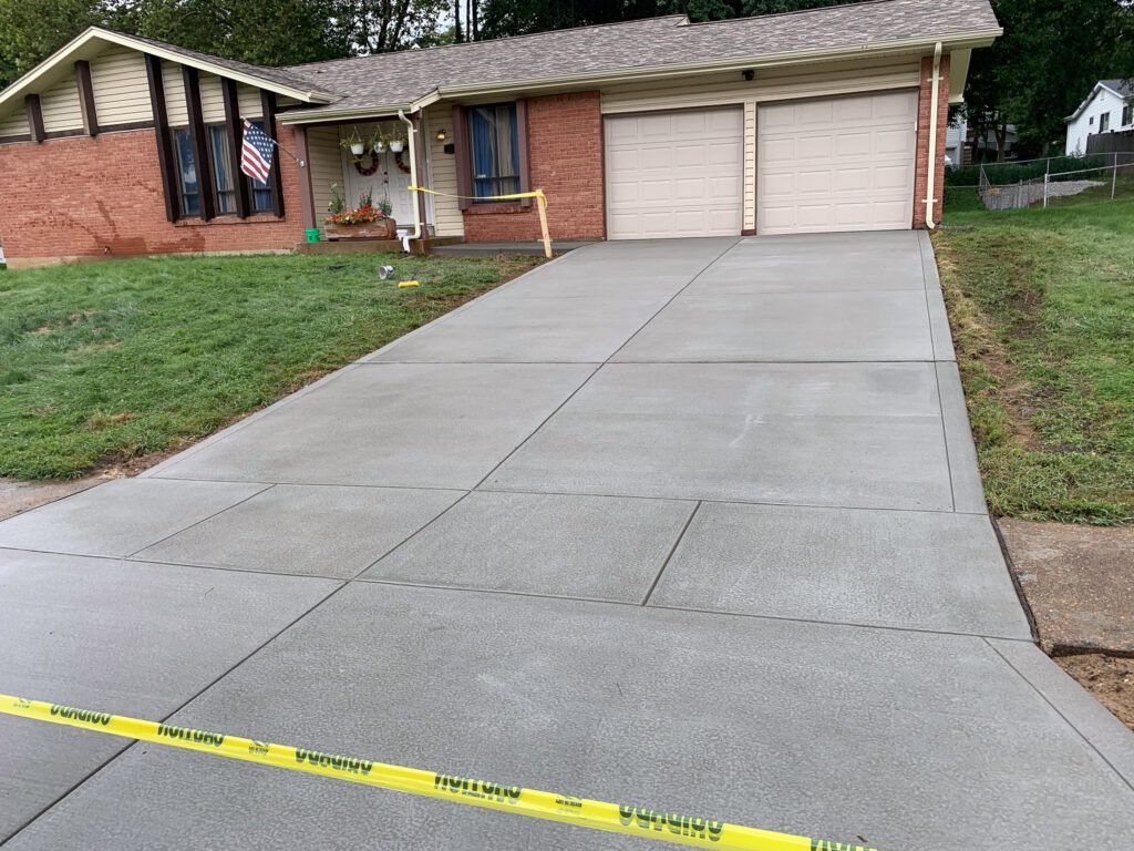 A concrete driveway leading to a house with two garage doors.