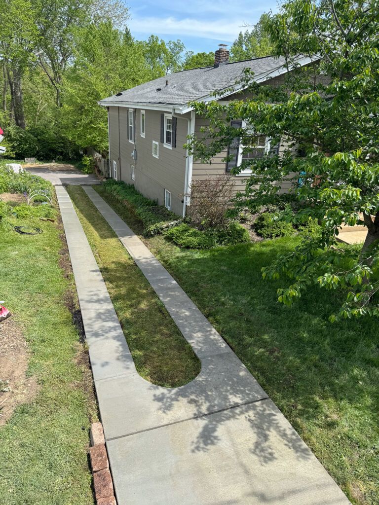 A sidewalk leading to a house with a lot of grass and trees.