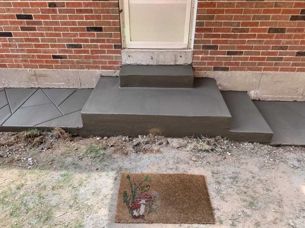 A brick building with concrete steps and a door mat in front of it.