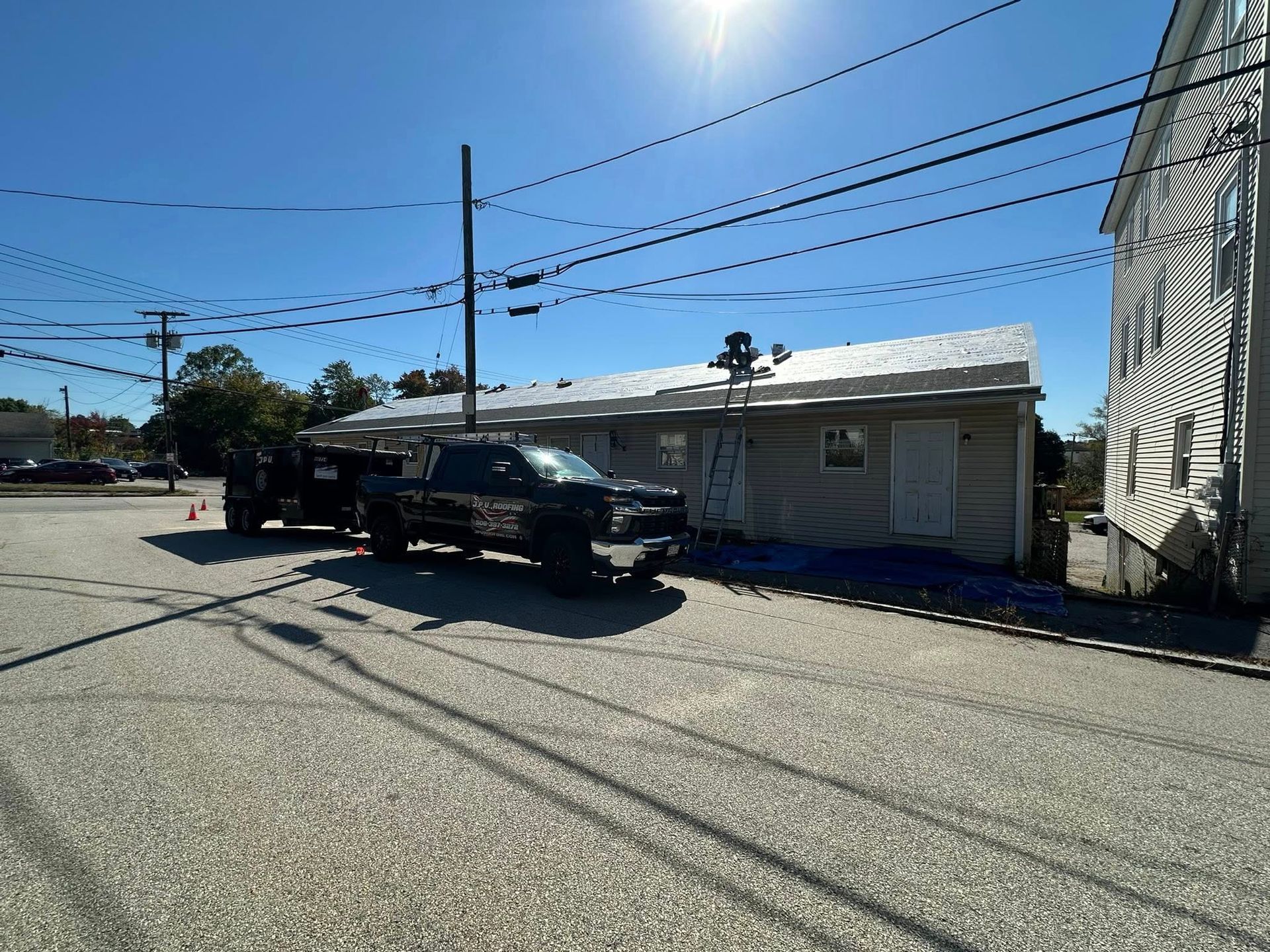 Truck with trailer parked near a building where roof work is in progress on a sunny day.