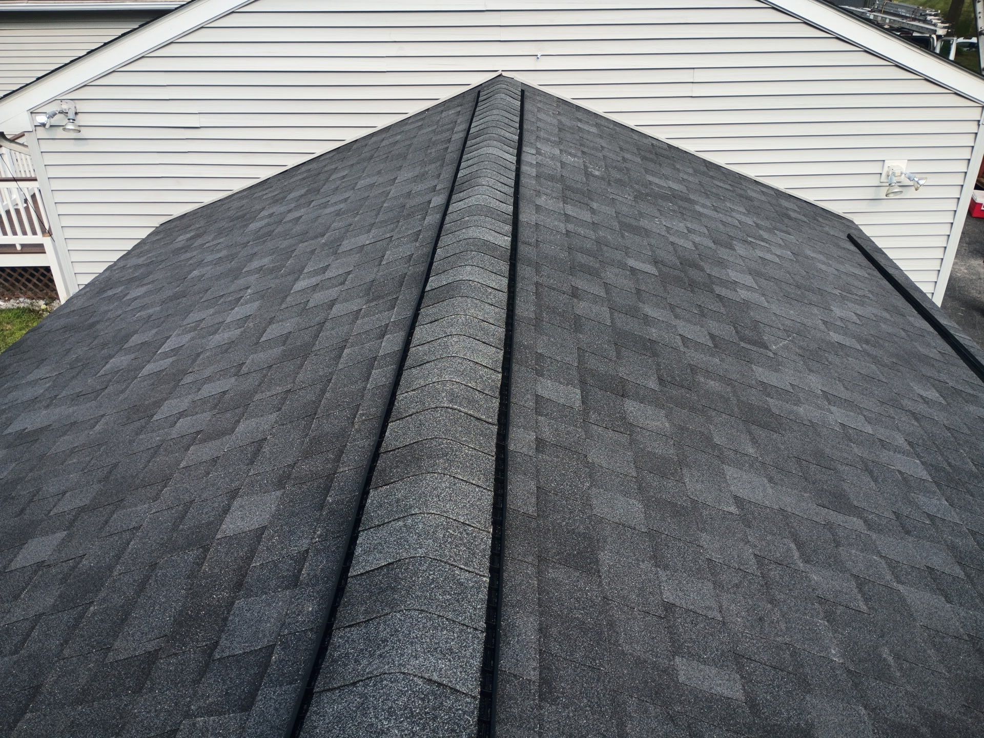 Dark asphalt shingle roof with a center ridge, viewed from above, against a light-colored siding.