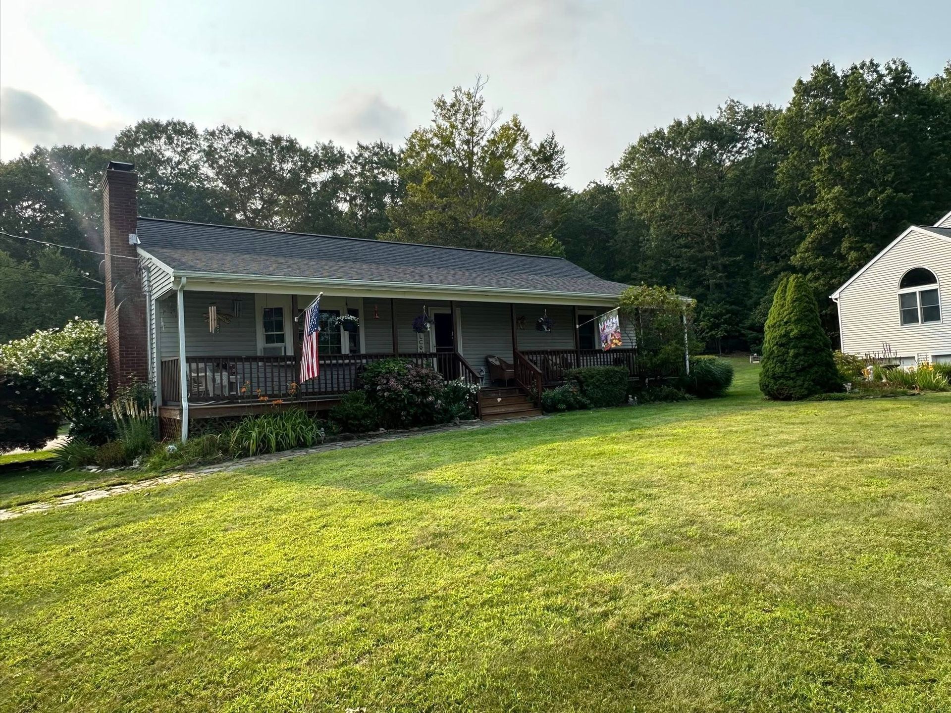 Ranch-style house with a porch on a grassy hill, with trees in the background.