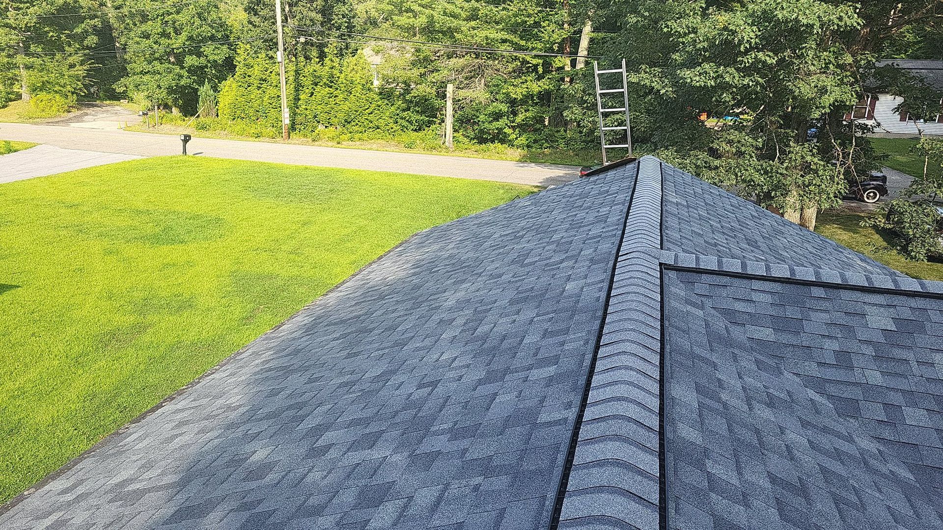 View from a roof with gray shingles, a ladder, and a green lawn in the background.